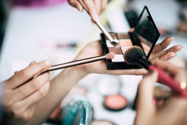 Mujeres haciendo maquillaje con cepillo y cosmetica.