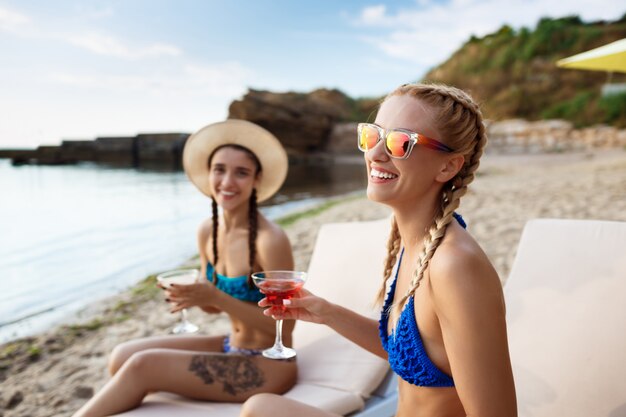 Mujeres hermosas jóvenes sonriendo, tomando el sol, tumbado en tumbonas cerca del mar