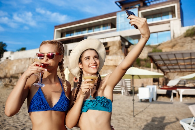 Mujeres hermosas jóvenes en traje de baño sonriendo, haciendo selfie en la playa