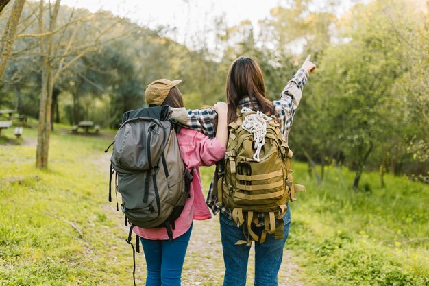 Mujeres irreconocibles con mochilas apuntando a la distancia