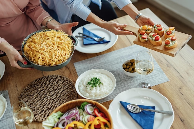 Mujeres irreconocibles sirviendo comida mientras preparan la mesa para el almuerzo.