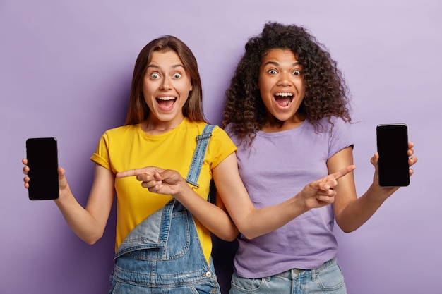 Mujeres jóvenes alegres apuntan a las pantallas de los teléfonos inteligentes