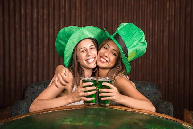 Mujeres jovenes alegres que abrazan con los vidrios de bebida en el sofá cerca de la tabla