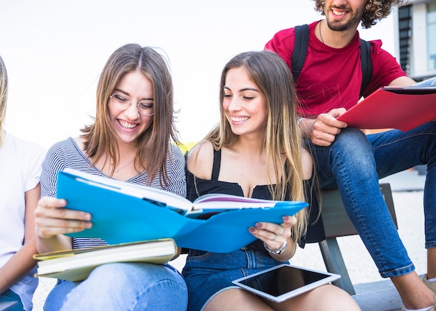 Foto gratuita mujeres jóvenes alegres que leen el libro de texto junto