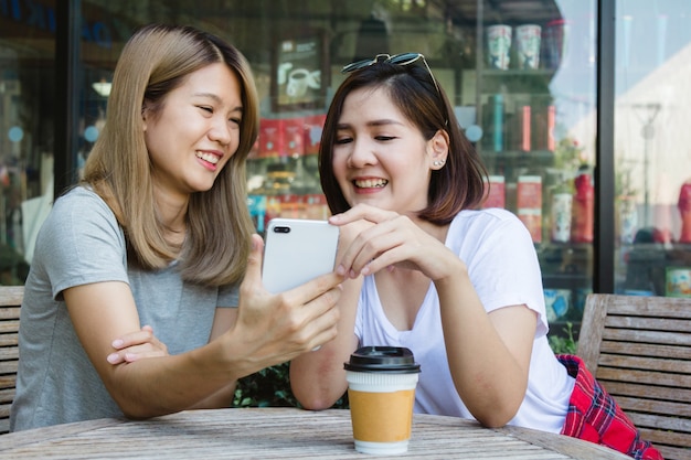 Mujeres jovenes asiáticas alegres que se sientan en café de consumición del café con los amigos y que hablan junto. Attrac