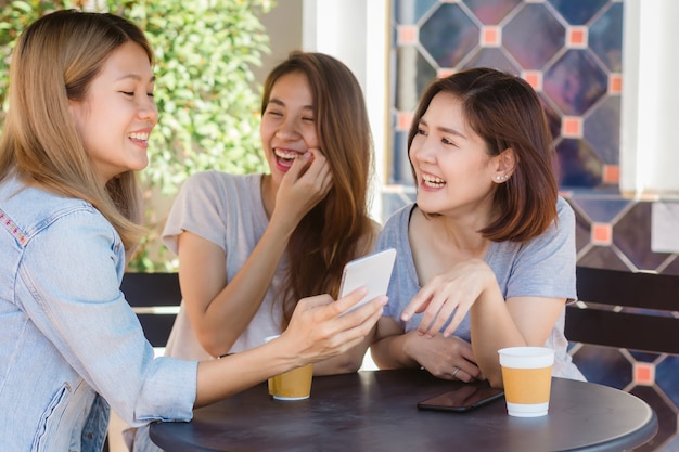 Mujeres jovenes asiáticas alegres que se sientan en café de consumición del café con los amigos y que hablan junto