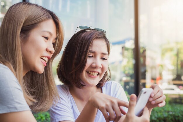 Mujeres jovenes asiáticas alegres que se sientan en café de consumición del café con los amigos y que hablan junto