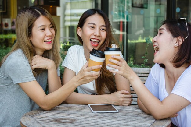 Mujeres jovenes asiáticas alegres que se sientan en café de consumición del café con los amigos y que hablan junto