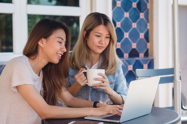 Mujeres jóvenes asiáticas en ropa casual elegante trabajando enviando correos electrónicos en computadoras portátiles y tomando café
