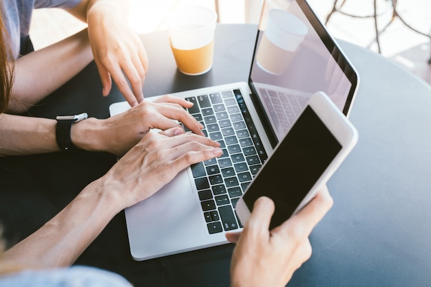 Mujeres jóvenes asiáticas trabajando en una computadora portátil usando y mirando un teléfono inteligente y tomando café