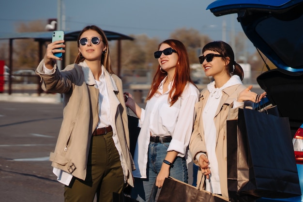 Mujeres jóvenes en el coche con bolsas de la compra. Chicas toman selfie