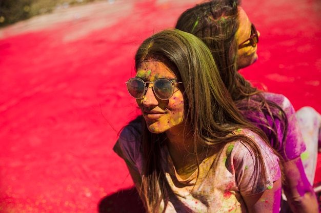 Mujeres jóvenes cubiertas de colores holi con gafas de sol sentadas espalda con espalda