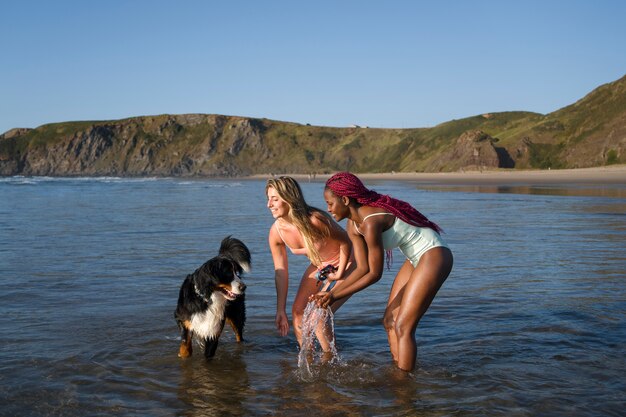 Mujeres jóvenes divirtiéndose con un perro en la playa