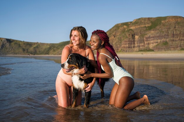 Mujeres jóvenes divirtiéndose con un perro en la playa