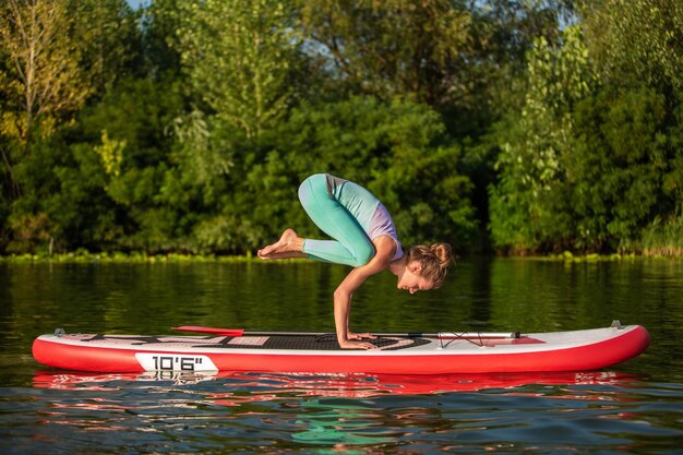 Las mujeres jóvenes están haciendo yoga en una tabla de remo SUP en un hermoso lago o río. El concepto de un estilo de vida saludable. Deporte. Yoga. Hobby