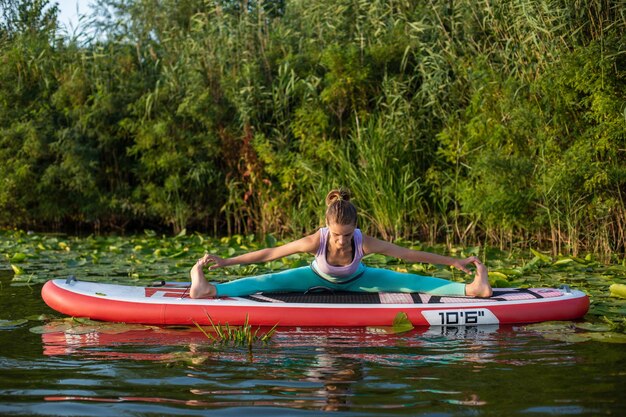 Las mujeres jóvenes están haciendo yoga en una tabla de remo SUP en un hermoso lago o río. El concepto de un estilo de vida saludable. Deporte. Yoga. Hobby