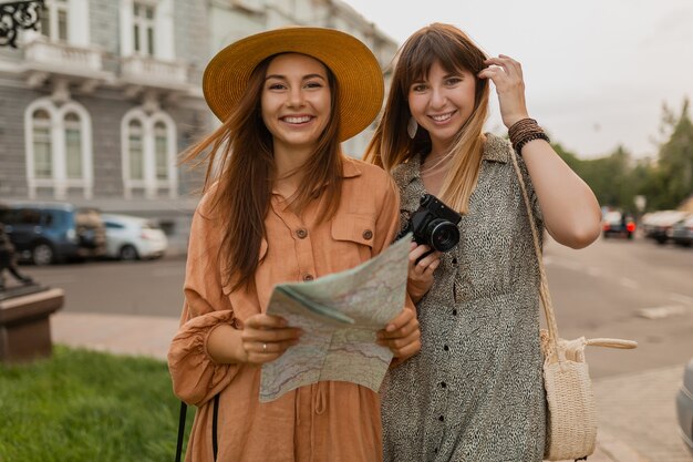 Mujeres jóvenes con estilo que viajan juntas en Europa vestidas con vestidos y accesorios de moda de primavera con mapa