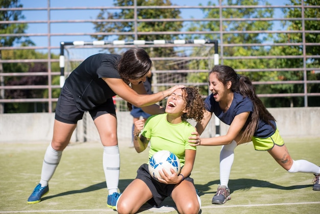 Mujeres jóvenes extasiadas celebrando la victoria. Deportistas con coloridos uniformes animando, felicitando a su compañero de equipo. Portero decepcionado en segundo plano. Deporte, ocio, concepto de estilo de vida activo.