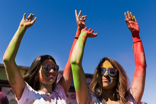 Mujeres jóvenes con gafas de sol disfrutando del festival holi contra el cielo azul