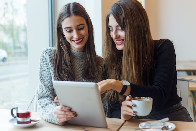 Mujeres jóvenes hermosas que usan la tableta digital en cafetería.