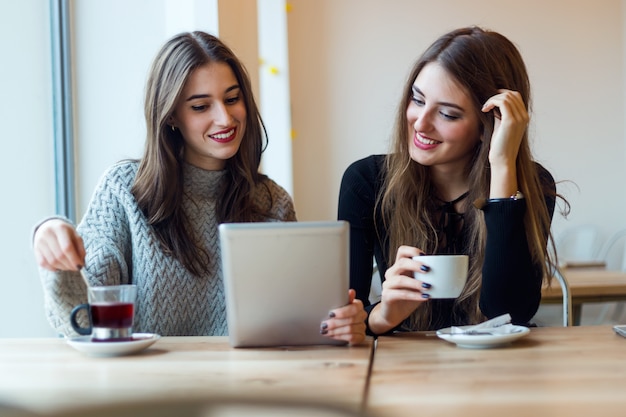 Mujeres jóvenes hermosas que usan la tableta digital en cafetería.