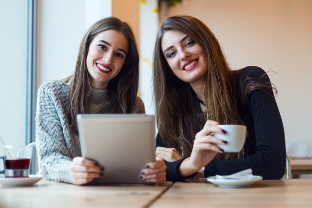 Mujeres jóvenes hermosas que usan la tableta digital en cafetería.