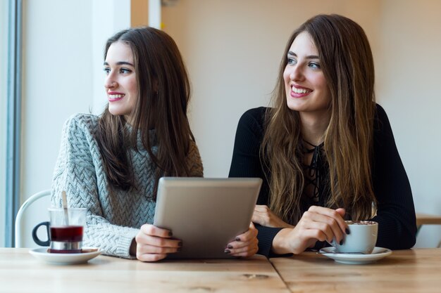 Mujeres jóvenes hermosas que usan la tableta digital en cafetería.