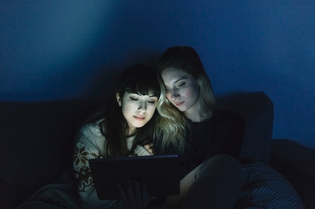 Mujeres jóvenes mirando tableta en la oscuridad