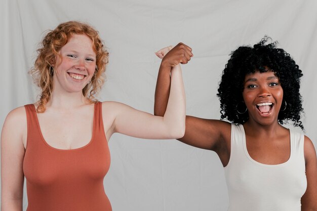 Foto gratuita mujeres jovenes multiétnicas alegres que torcen sus manos que se oponen al contexto gris