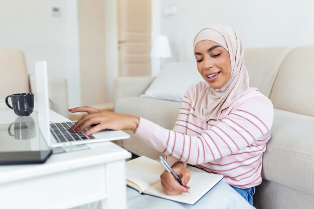 Las mujeres jóvenes musulmanas usan hiyab escribiendo y revisando el pedido de la dirección del cliente en la computadora portátil en casa por la mañana Concepto de negocio pequeño y compra en línea