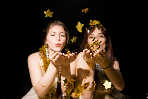 Mujeres jóvenes con oropel que sopla sobre adornos de papel estrellas