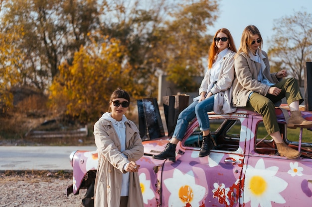 Mujeres jóvenes posando cerca de un viejo coche decorado