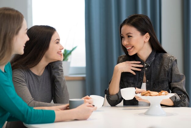 Mujeres jóvenes positivas tomando café y sonriendo