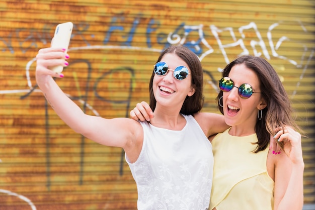 Mujeres jovenes que toman el selfie mientras que se coloca en la calle urbana