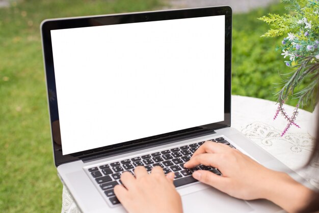 Mujeres jovenes que usan la computadora portátil en la tabla en el jardín. vista lateral. simula espacio libre en la pantalla para su diseño