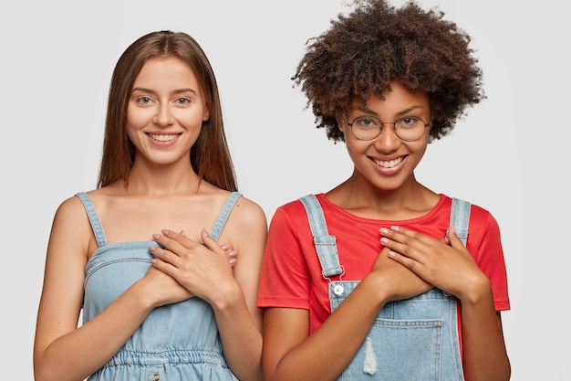 Las mujeres jóvenes de raza mixta de buen corazón mantienen las manos en el pecho