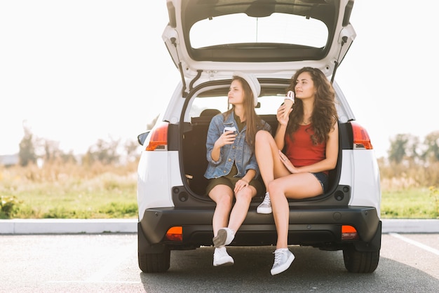 Mujeres jóvenes sentadas en el baúl del auto