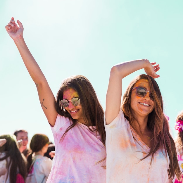 Mujeres jóvenes sonrientes con gafas de sol bailando en el festival holi
