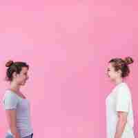 Foto gratuita mujeres jóvenes sonrientes de pie cara a cara mirando el uno al otro sobre fondo rosa