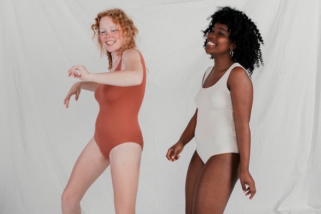 Foto gratuita mujeres jovenes sonrientes que bailan contra el contexto gris