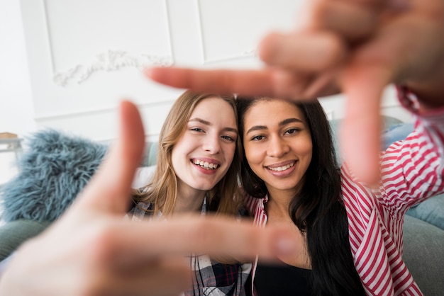 Mujeres jovenes sonrientes que hacen el marco de la foto con las manos