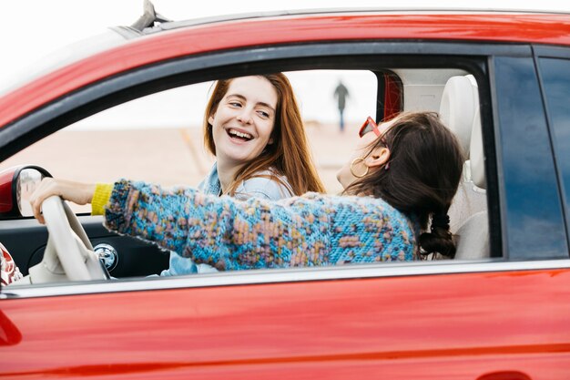 Mujeres jovenes sonrientes que se sientan en coche