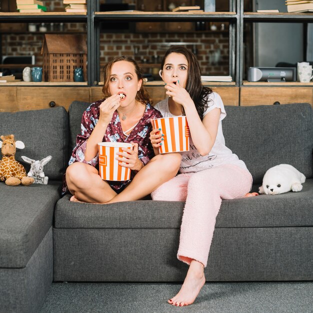 Mujeres jóvenes sorprendidas sentado en el sofá viendo la televisión