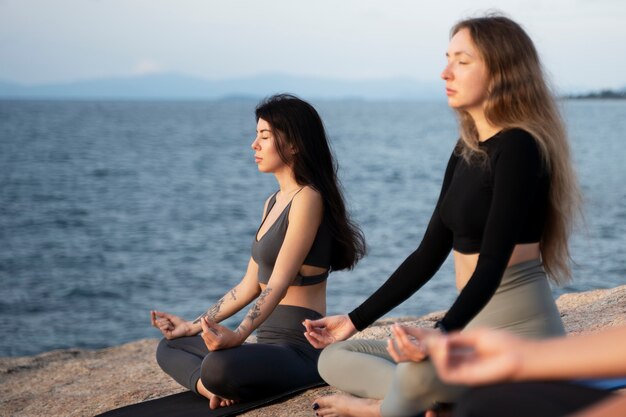 Mujeres jóvenes de tiro completo meditando en la alfombra afuera