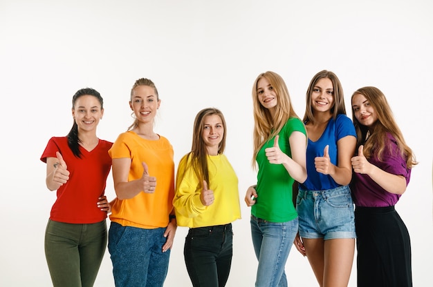 Las mujeres jóvenes vestían los colores de la bandera LGBT aislados en la pared blanca. modelos femeninos con camisas brillantes.