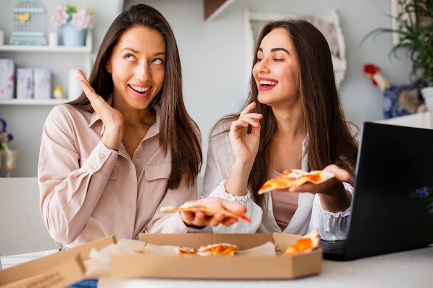 Mujeres juguetonas comiendo pizza en casa