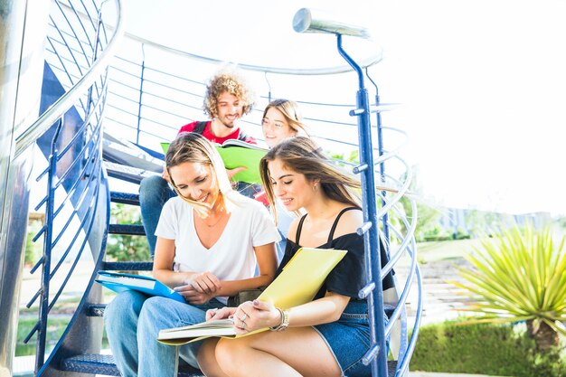 Mujeres leyendo libros de texto en la escalera cerca de amigos