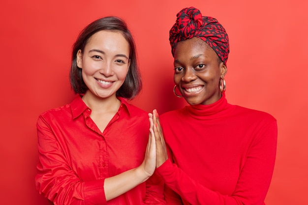 las mujeres mantienen las palmas juntas muestran apoyo mutuo y comprensión del trabajo mientras el equipo sonríe agradablemente parados hombro con hombro en rojo