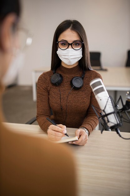 Mujeres con máscaras médicas haciendo un programa de radio.