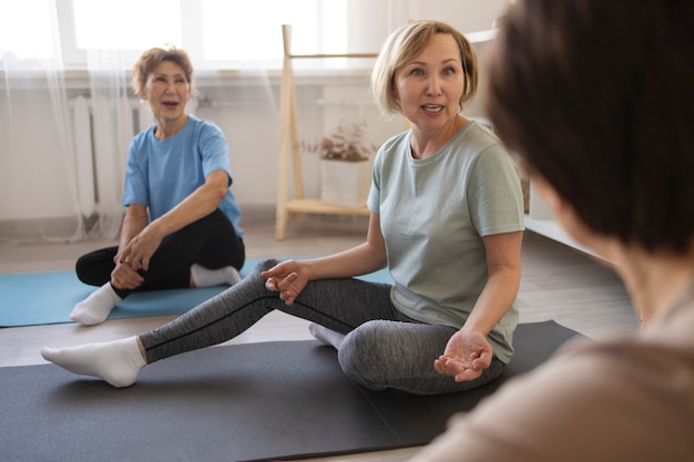 Mujeres mayores haciendo yoga en casa y hablando entre ellas